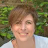 Frontal de Mariana Ierocades. Mariana sonríe a la cámara, con un fondo natural de hojas verdes y un muro de ladrillos. Lleva el cabello corto y luce una camiseta clara, con un gesto amigable y relajado.